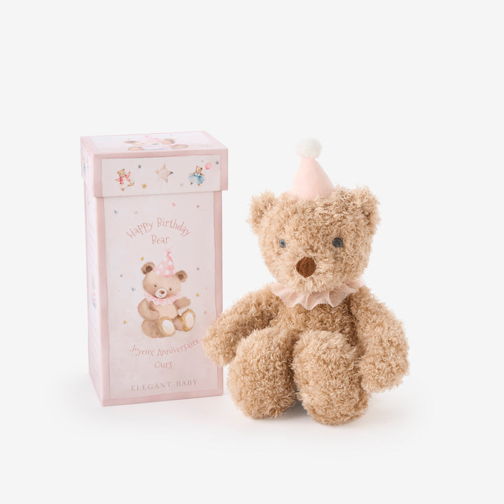 Teddy bear with a birthday hat next to a gift box on a white background