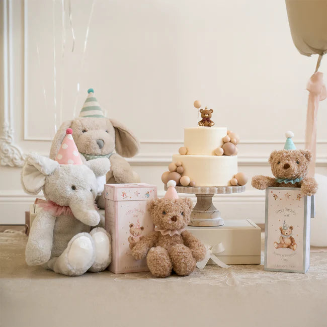 Children's toys including teddy bears, an elephant, and a cake on a decorative stand in a room.