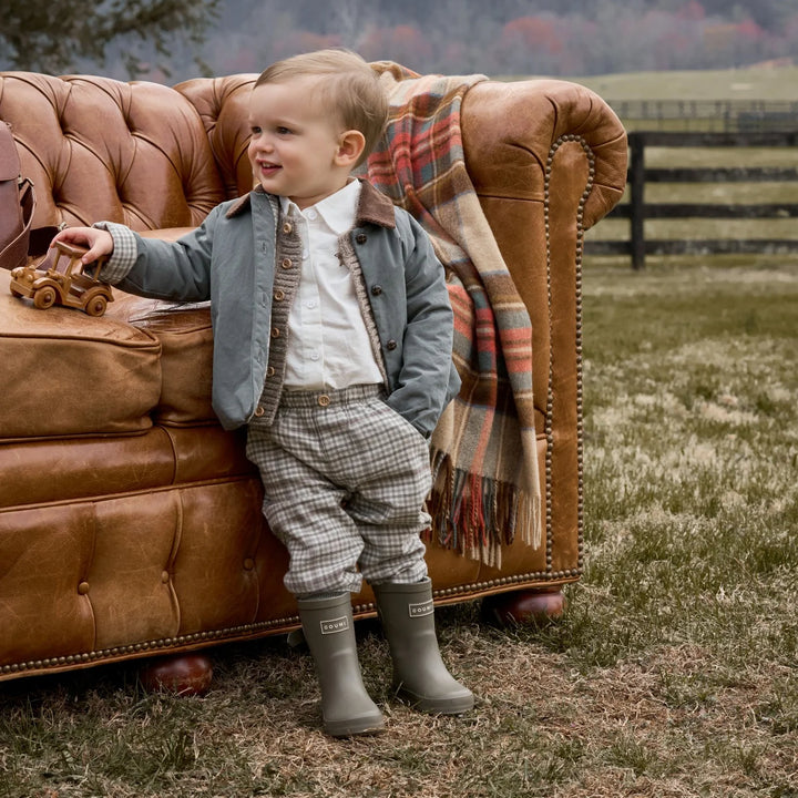 Child in formal attire standing next to a brown leather sofa outdoors.