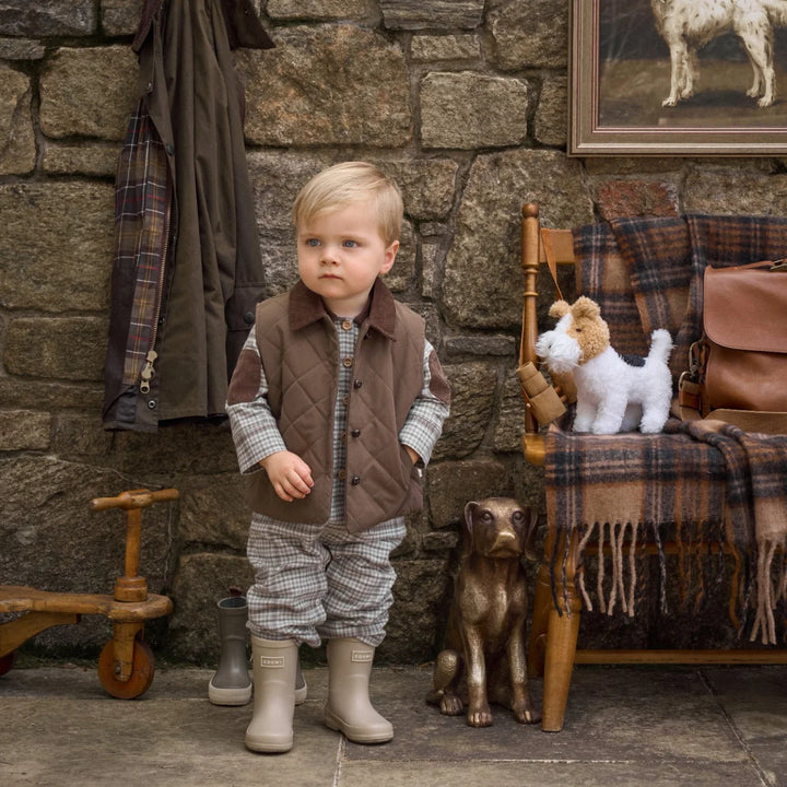 Young boy in plaid outfit standing in front of a stone wall with rustic decor.