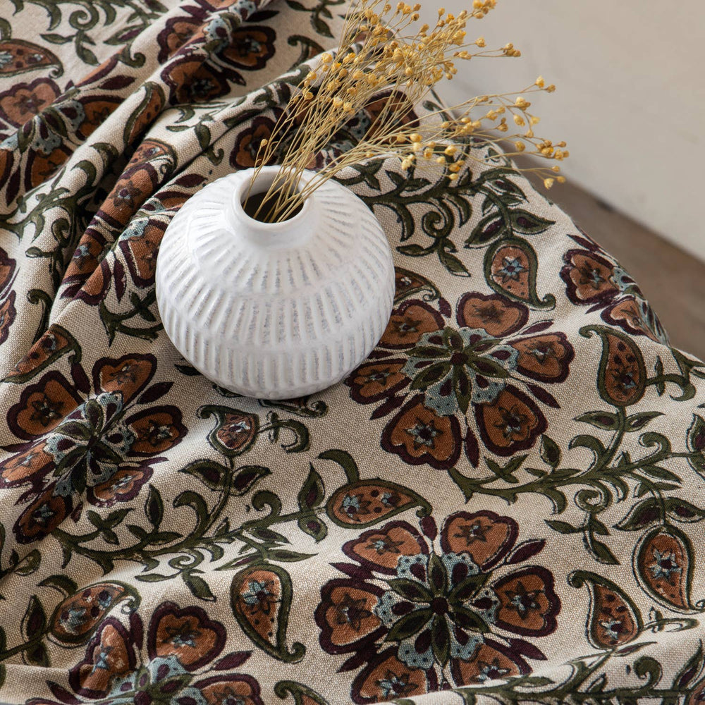 White vase with dried flowers on a floral-patterned fabric surface