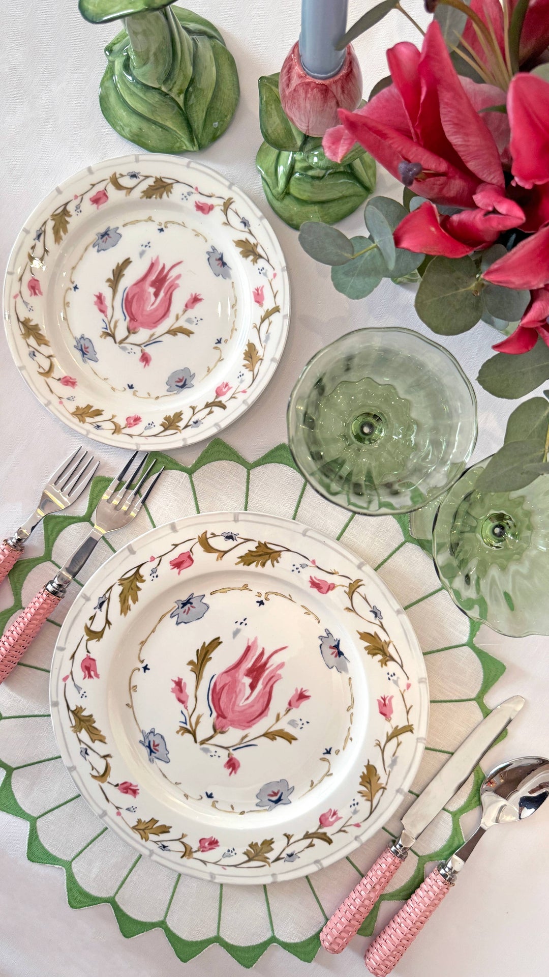Decorative table setting with floral plates, pink flowers, and green glasses.