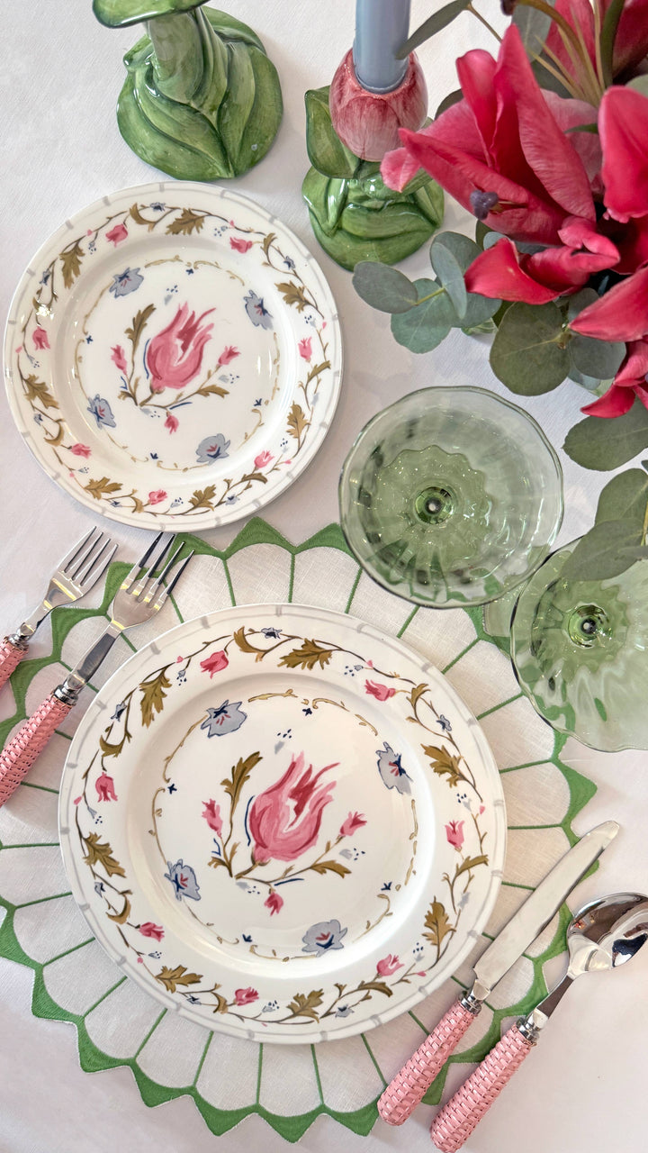 Decorative table setting with floral plates, pink flowers, and green glasses.