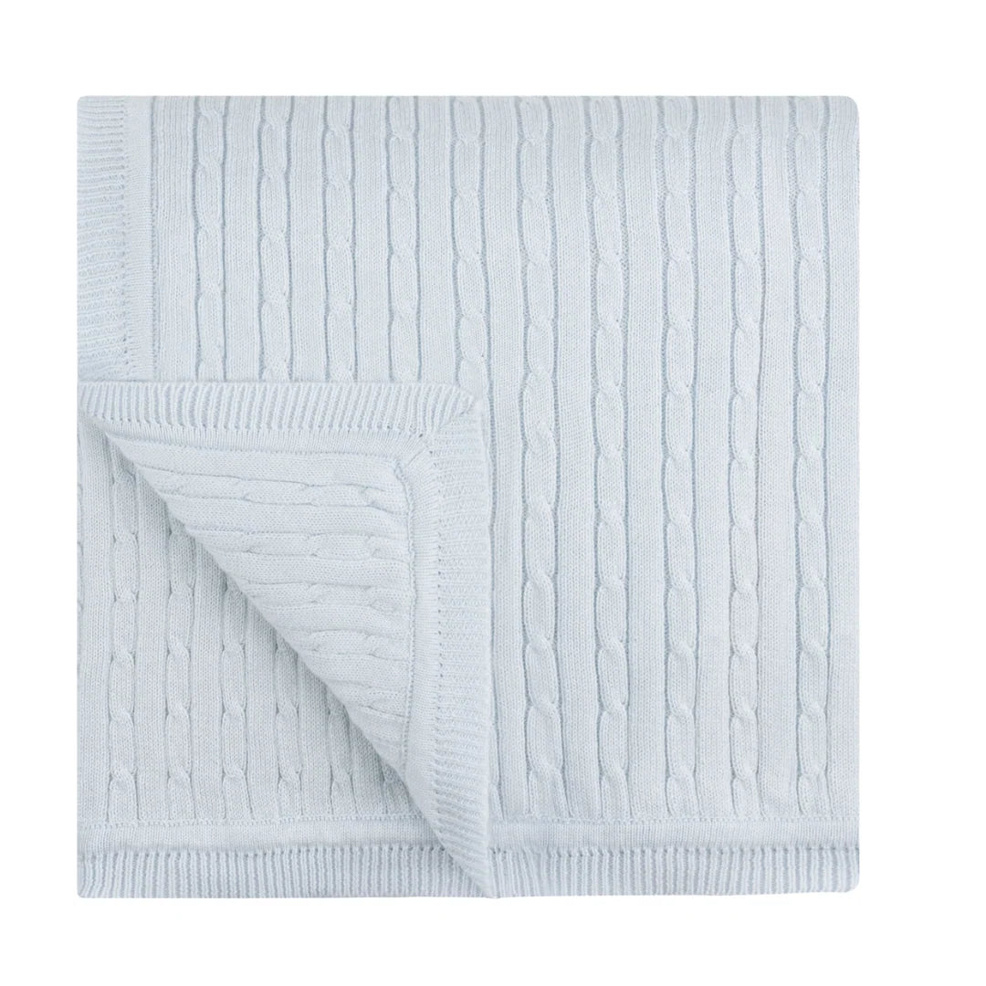 A light blue cable-knit blanket with a folded corner showing the ribbed reverse side, photographed on a solid white background.