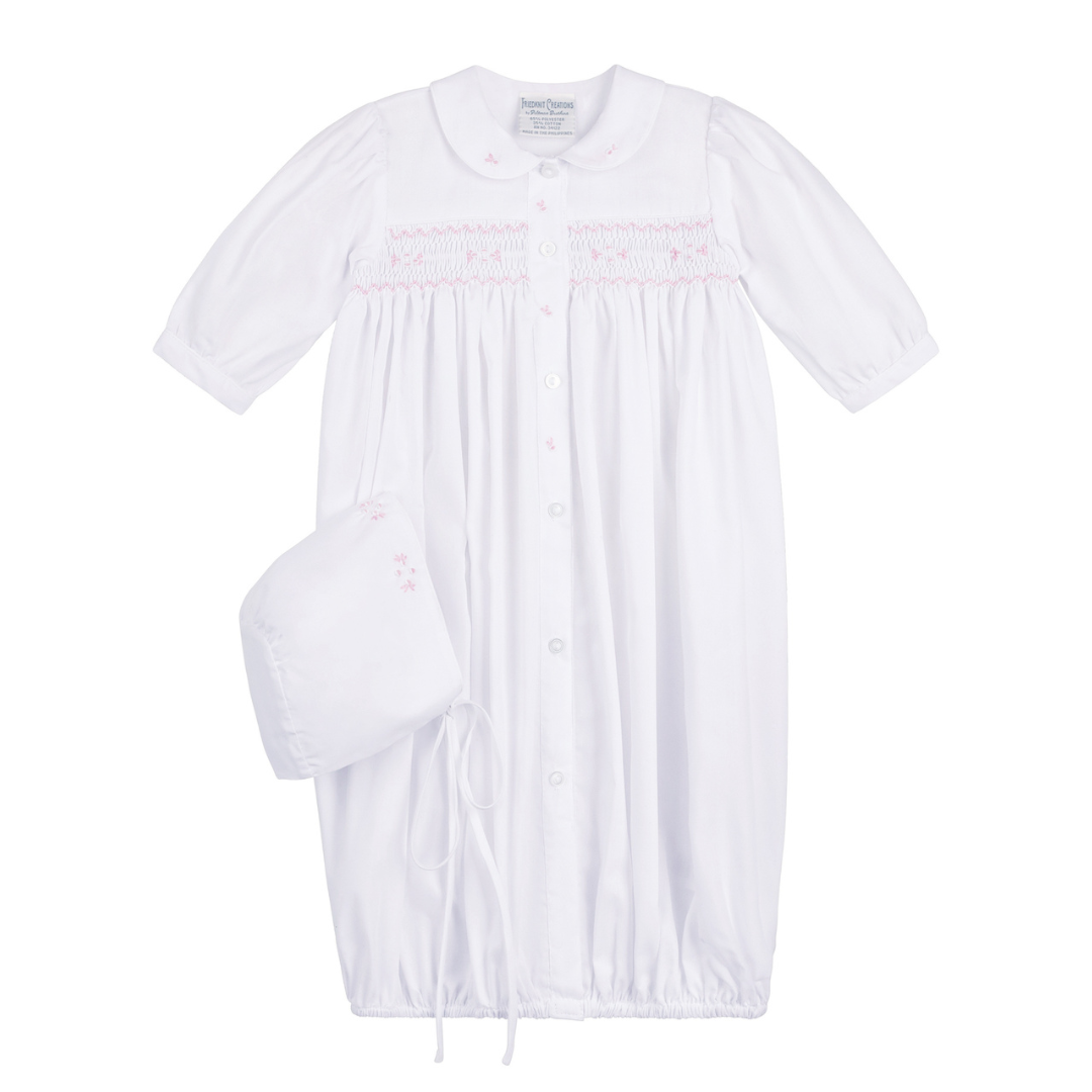 White baby dress with pink embroidery and matching bonnet on a white background