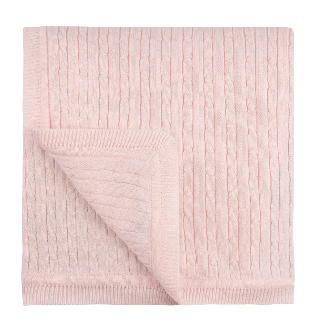 A light pink cable-knit blanket with ribbed borders, folded to show its texture and reverse side, on a solid white background.