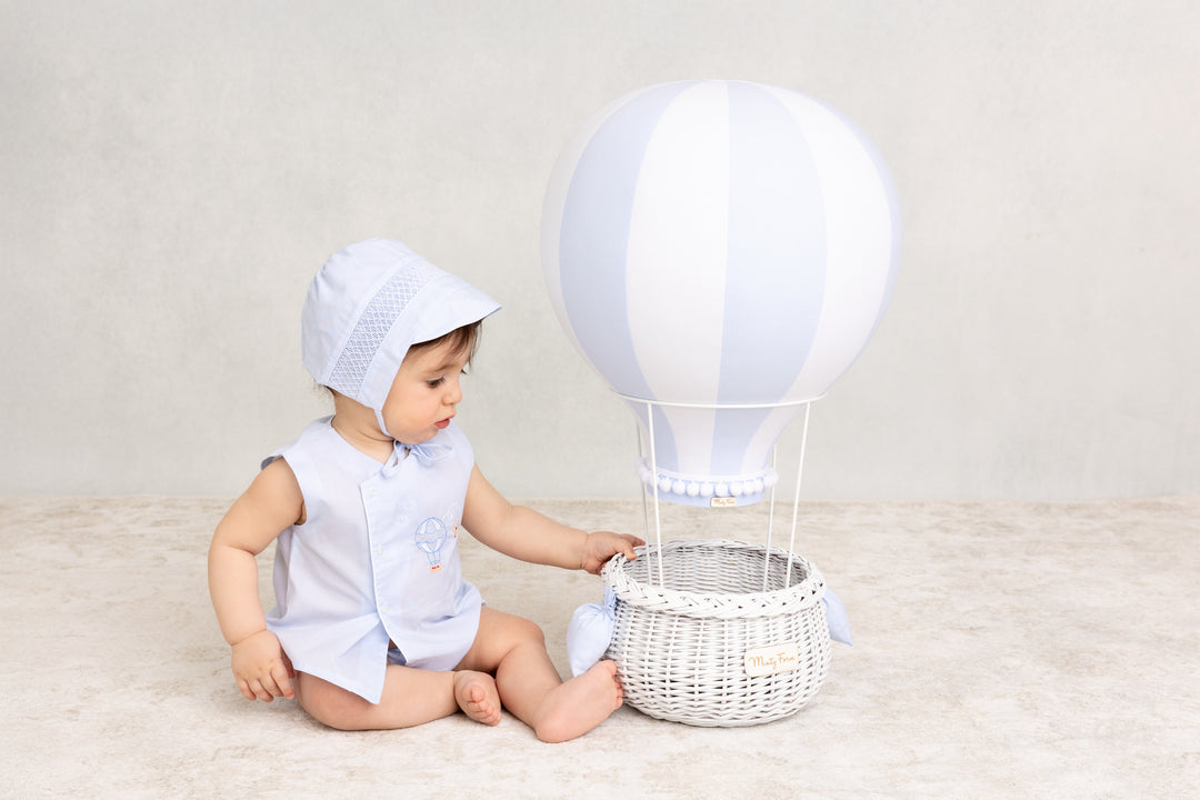baby boy dressed in feltman brothers diaper set with embroidered hot air balloon sits next to a hot air balloon prop 