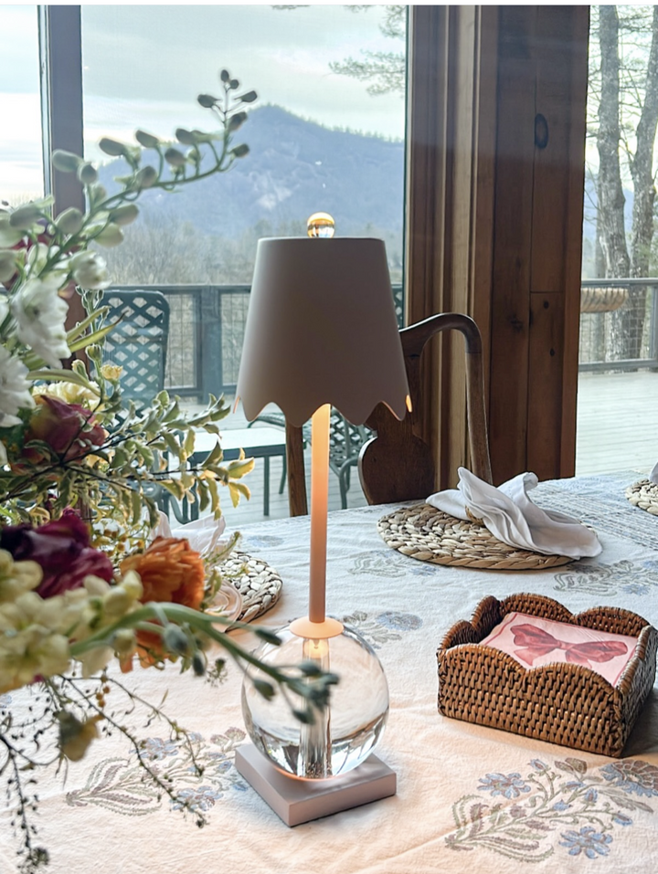 Decorative table setting with a lamp, flowers, and a heart-shaped box in a room with a mountain view.
