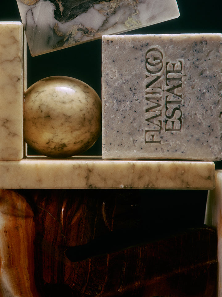 A close-up of a carved stone slab with the words 'FLAMING ESTATE' embossed vertically, alongside other polished stone objects and a dark background.
