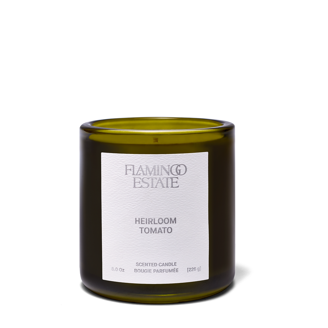 An amber glass candle jar with a white label reading 'FLAMING ESTATE' and 'SAPPHO FIG' on a clean white background.