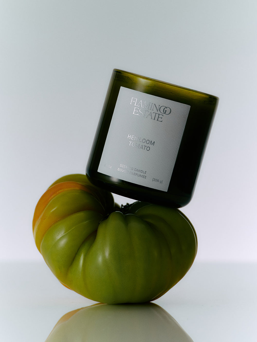 Candle in a green glass container with a label, placed on a decorative gourd against a white background.