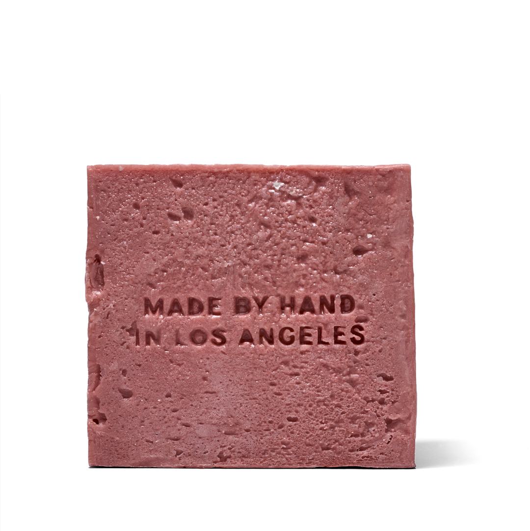 A single rectangular bar of dusty rose soap with a textured, stone-like surface embossed with the text 'MADE BY HAND IN LOS ANGELES' on a clean white background.