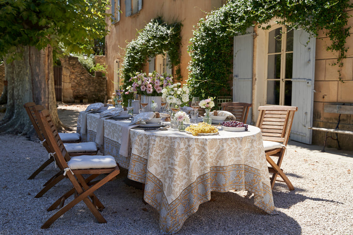 Outdoor dining setup with a table, chairs, and floral arrangements in a sunlit courtyard.