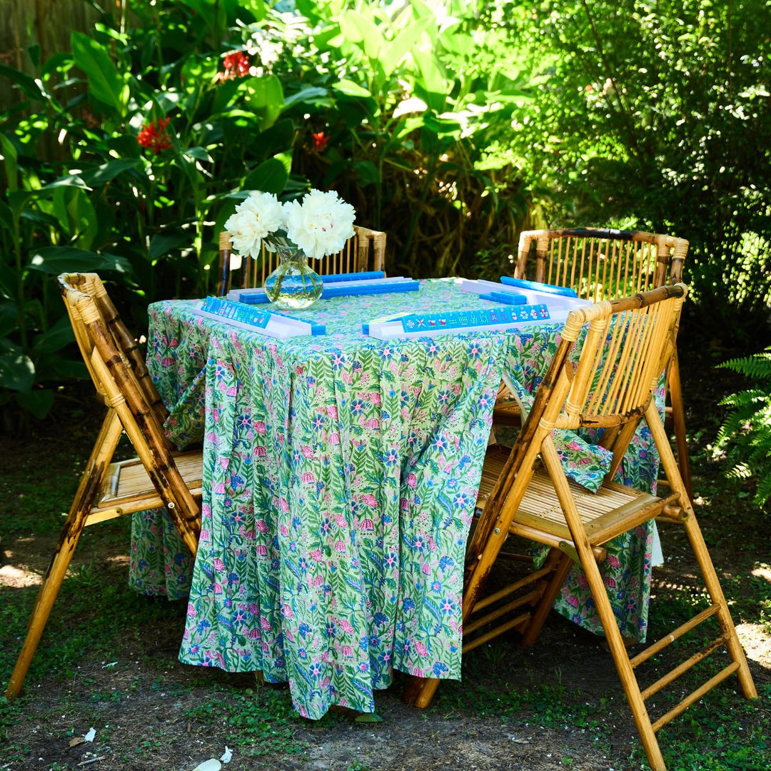 Outdoor setting with a floral tablecloth on a round table surrounded by wooden chairs.
