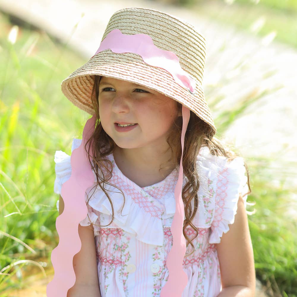 Young girl wearing a straw hat with pink ribbon in a grassy outdoor setting