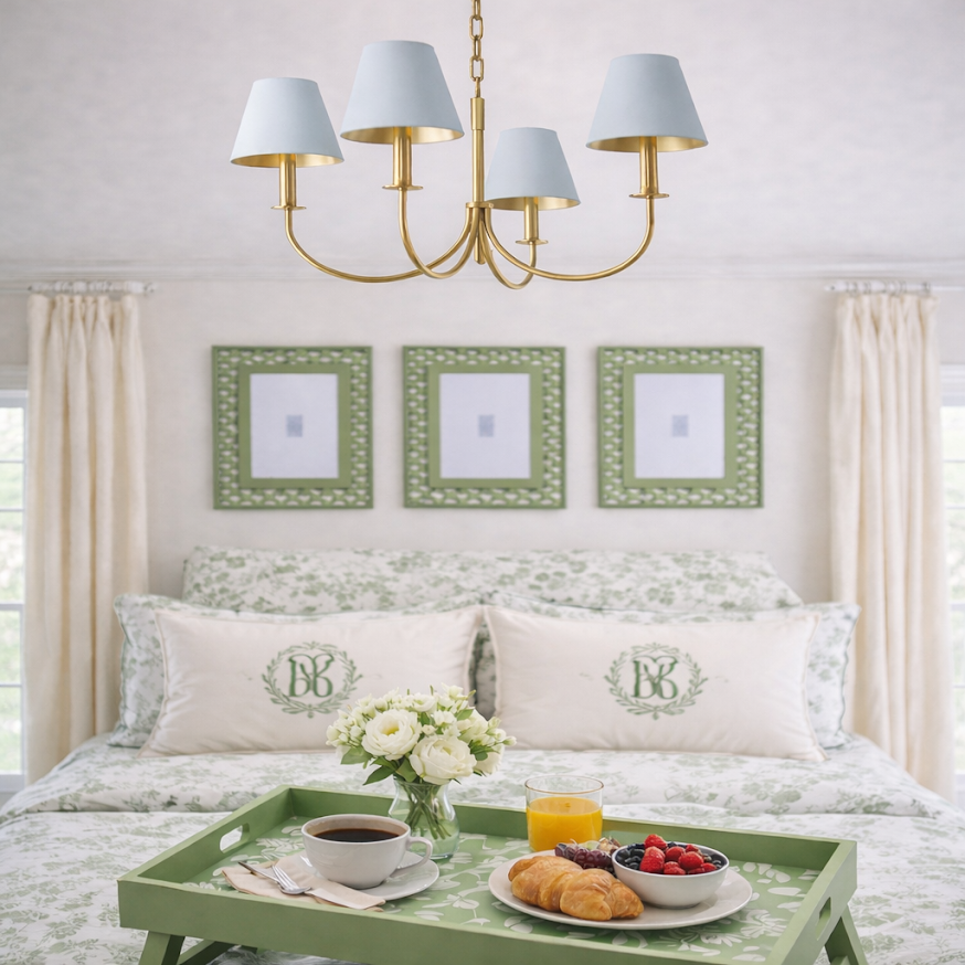 Bedroom with a tray of food and drinks on a green tray, floral arrangement, and decorative pillows.