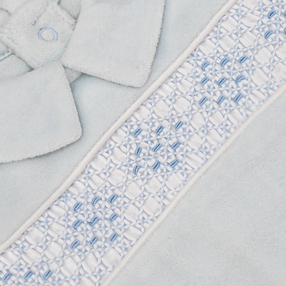 Close-up of a light blue plush fabric item, likely a soft accessory or garment, featuring a decorative white and light blue embroidered border with a small button detail.