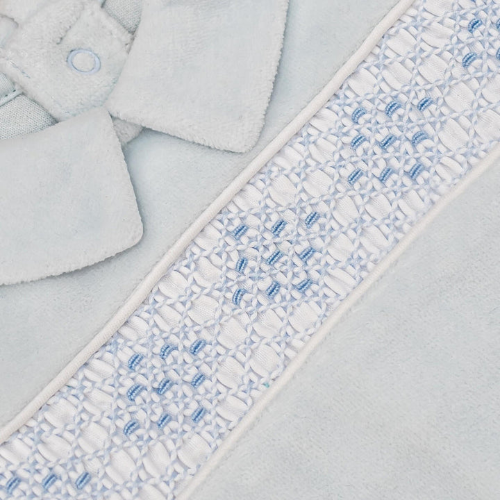 Close-up of a light blue plush fabric item, likely a soft accessory or garment, featuring a decorative white and light blue embroidered border with a small button detail.