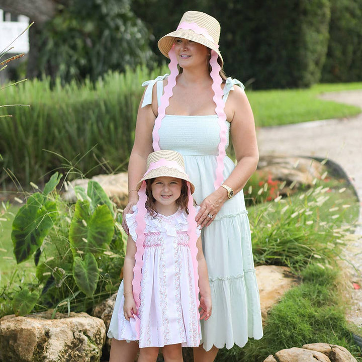 Woman and child in matching dresses with pink ribbons standing outdoors.