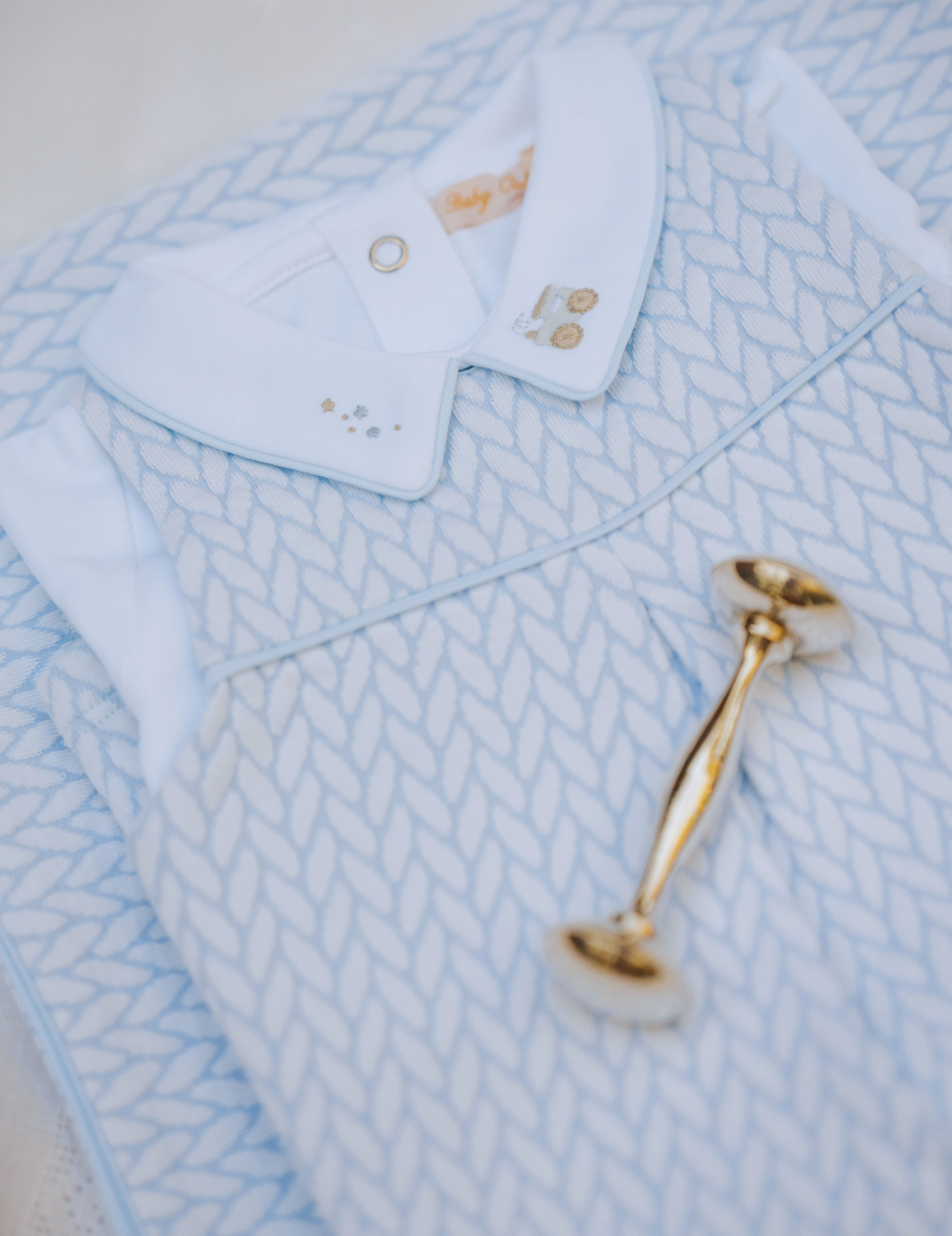 Close-up of a baby outfit with a blue and white patterned shirt and pants, featuring a gold stroller toy.