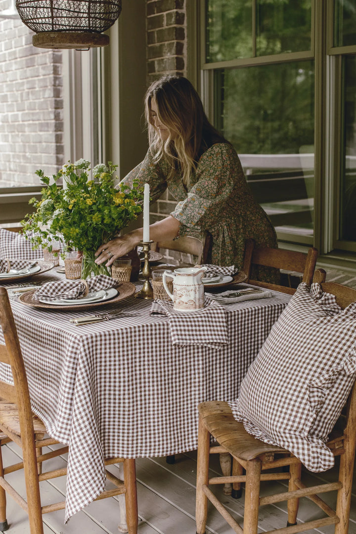 Woman setting a table with a checkered tablecloth and decorative elements.