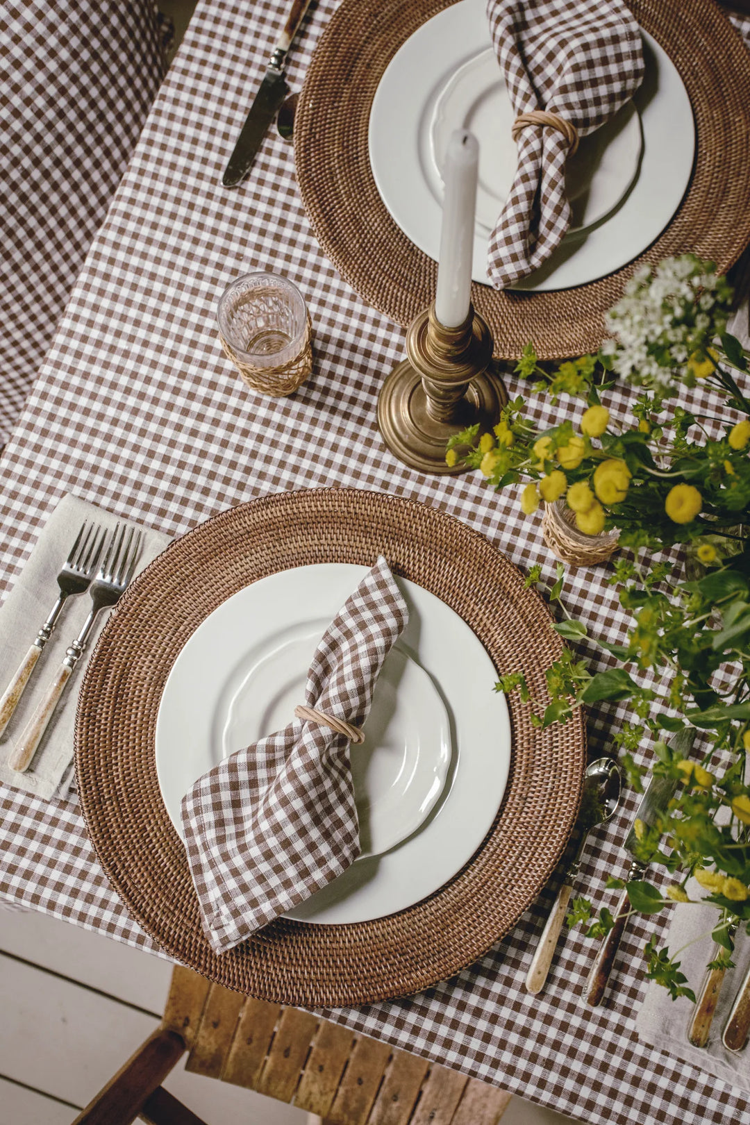 Elegant table setting with woven placemats, checkered tablecloth, and white plates.