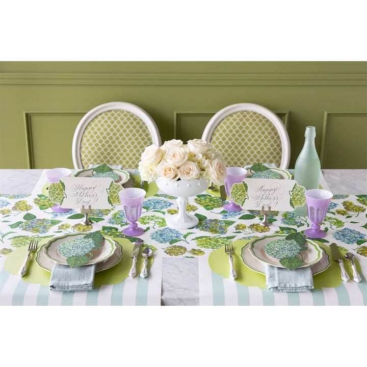 Elegant table setting with floral centerpiece, place cards, and decorative plates on a green wall background.