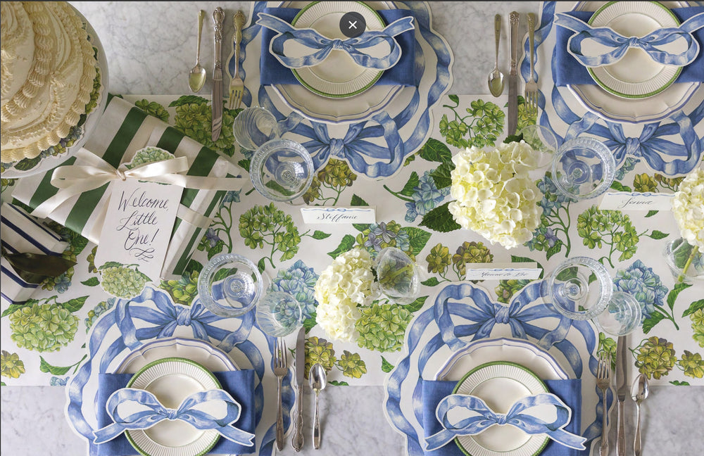 Table setting with blue and white napkins, silverware, and floral tablecloth.