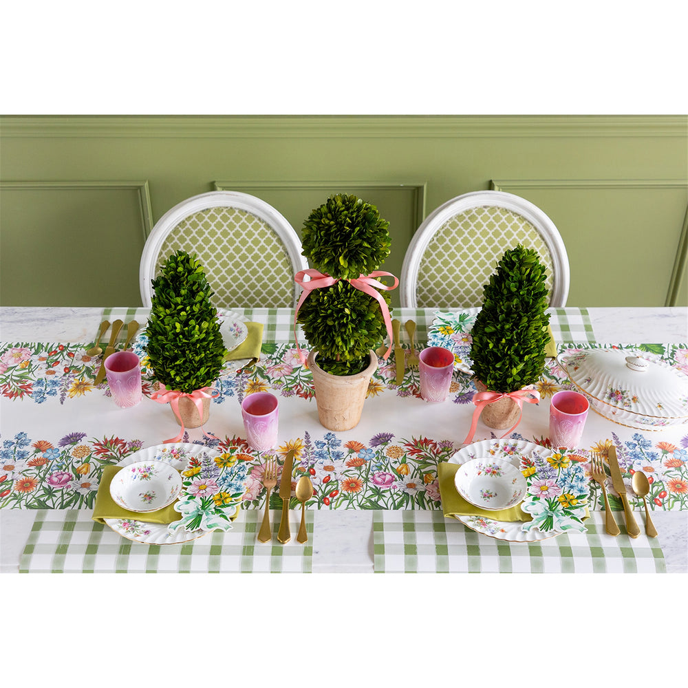 Dining table set with floral tablecloth, green centerpieces, and pink cups.
