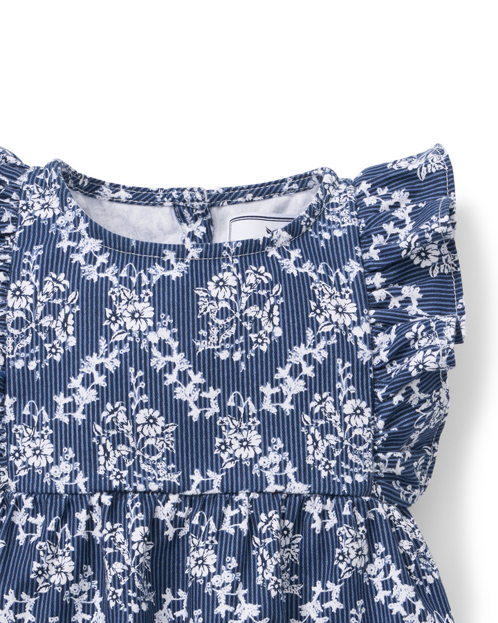Close-up of a children's clothing with a navy blue and white floral print over a fine vertical stripe background, featuring ruffled sleeves and a tiered skirt.