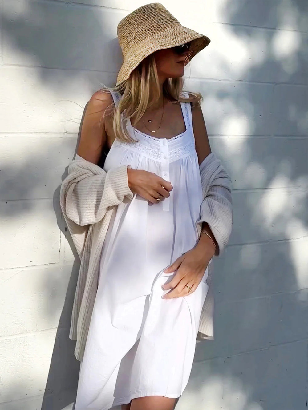 Woman wearing a white dress and straw hat against a light background