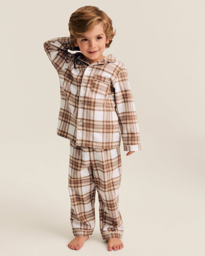 A young child wearing a two-piece pajama set with a brown and white plaid pattern, standing against a solid light beige background.