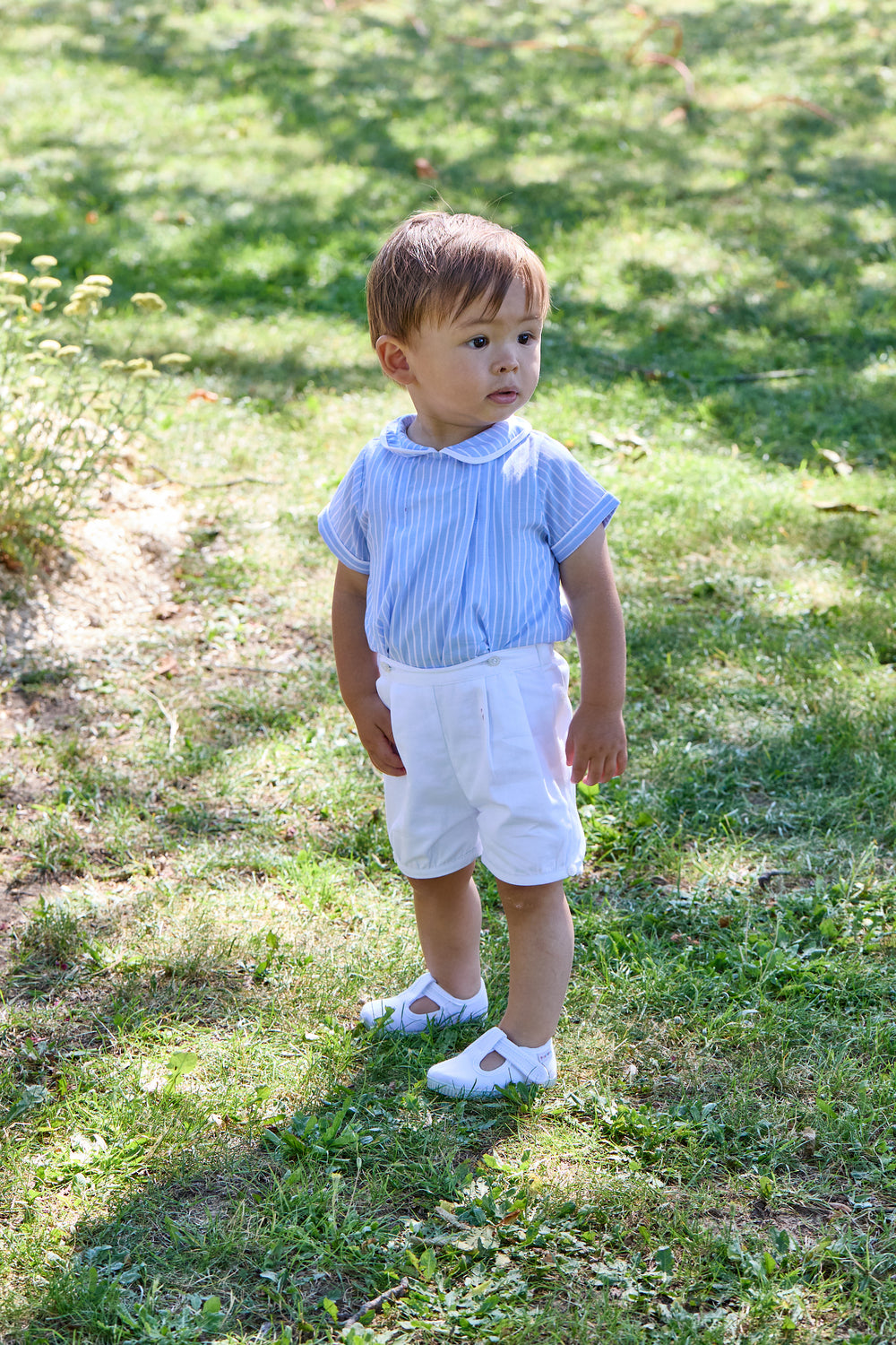 Child wearing a blue striped shirt and white shorts standing on grass