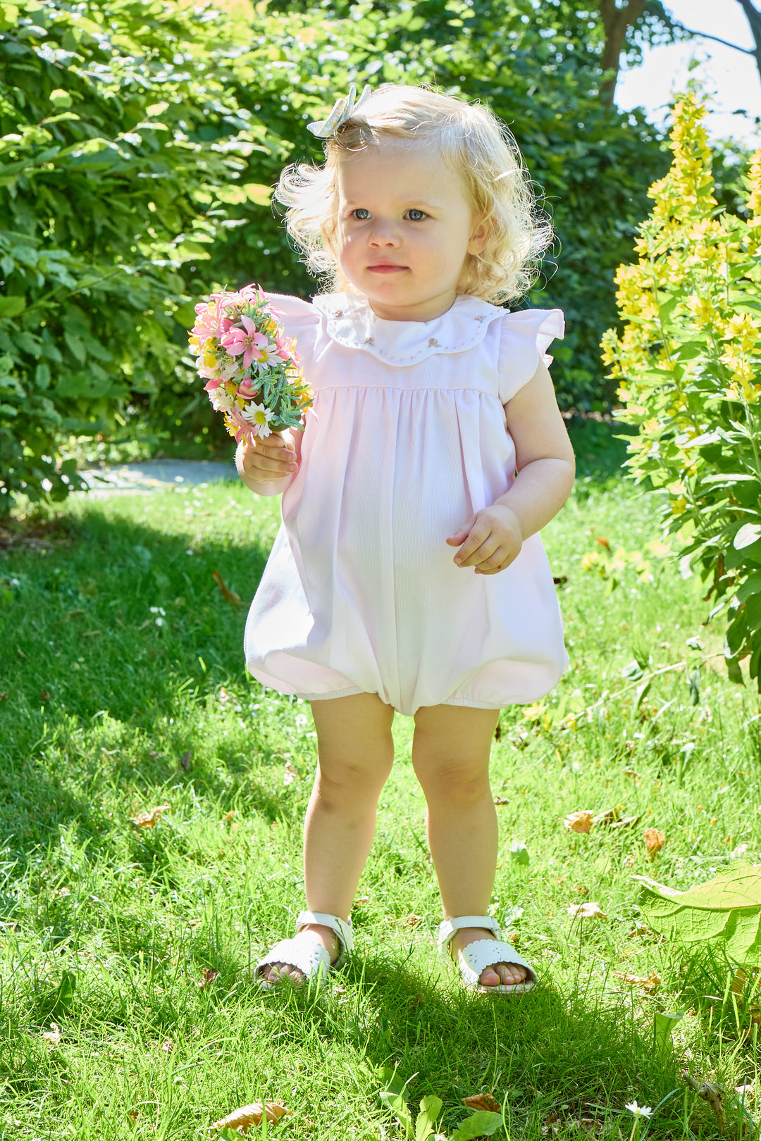 Young girl in a pink romper flowers in a garden