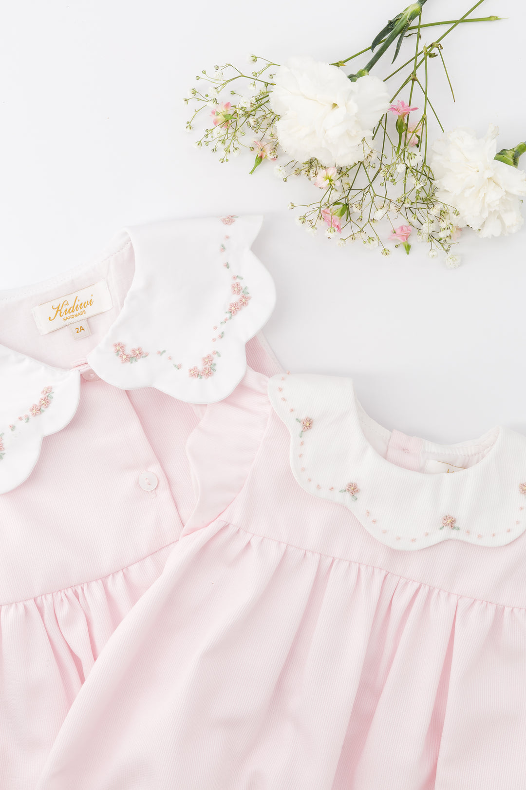 Pink baby dress with lace details and a bouquet of flowers on a white background