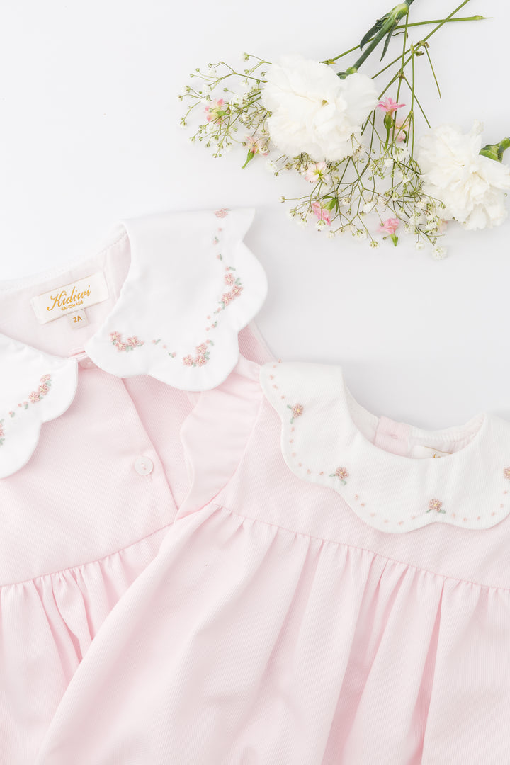 Pink baby dress with lace details and a bouquet of flowers on a white background