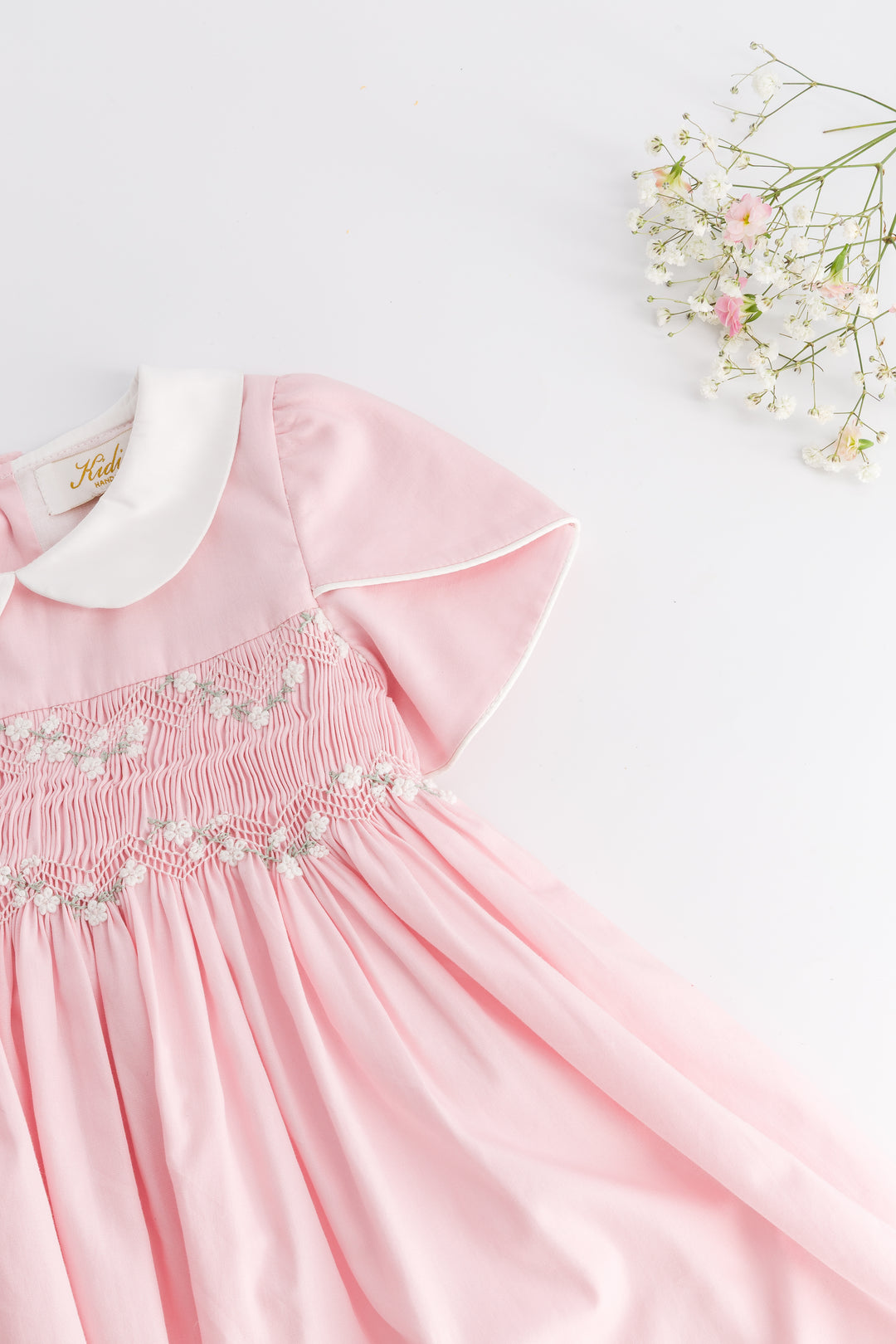 Pink dress with white collar and floral embroidery on a light background