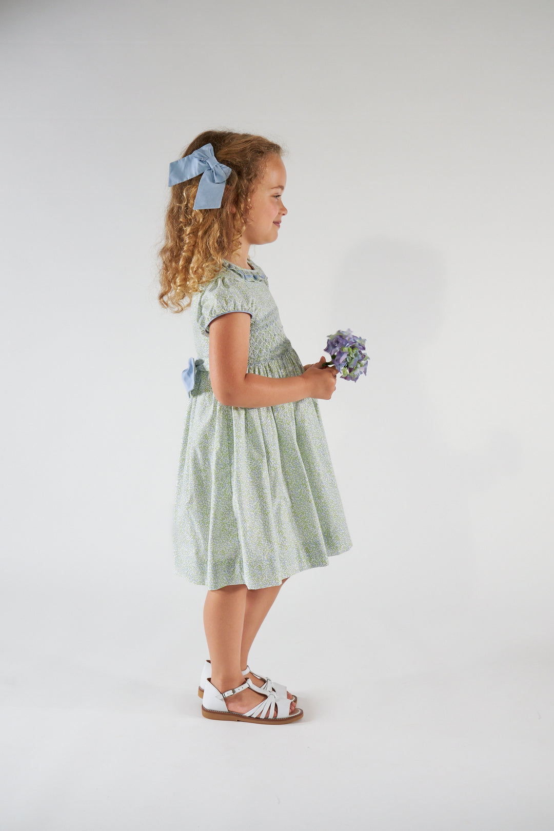 Young girl in a light green dress holding flowers against a white background