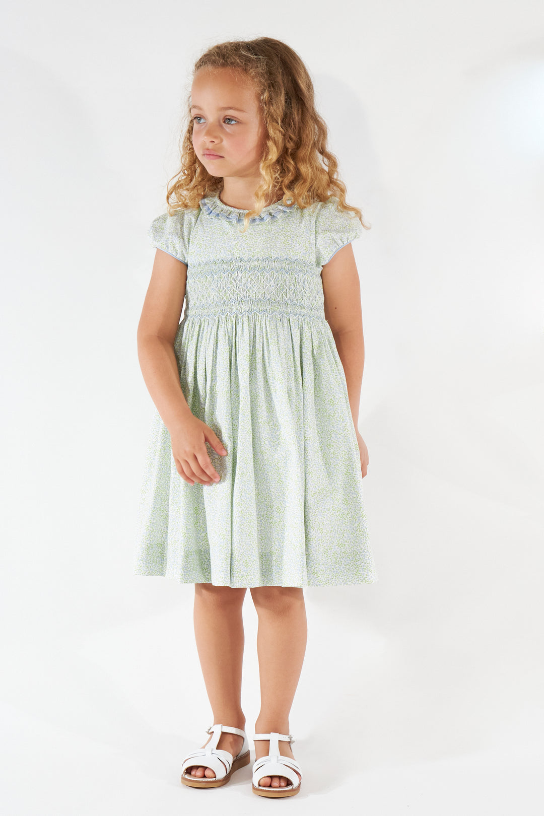 Young girl wearing a light green dress with floral patterns on a white background