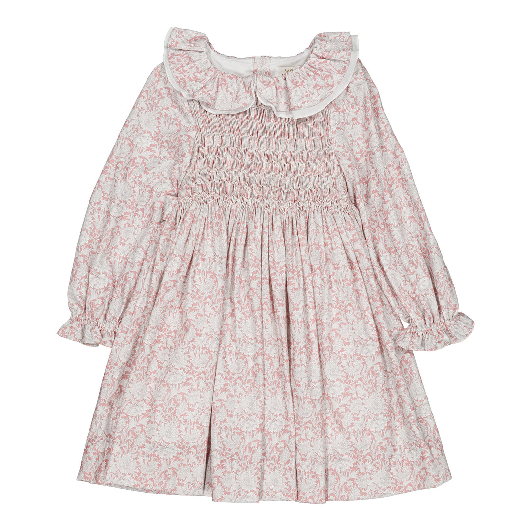 A long-sleeve baby dress with a pink floral toile pattern on a white background, featuring a smocked bodice, ruffled collar, and gathered sleeves.