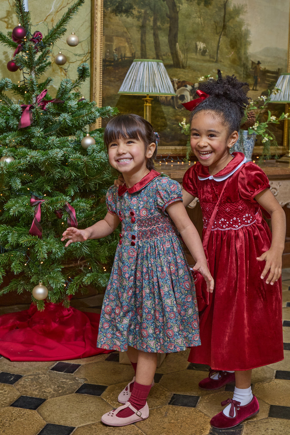 Two girls dressed in holiday dresses in front of christmas tree