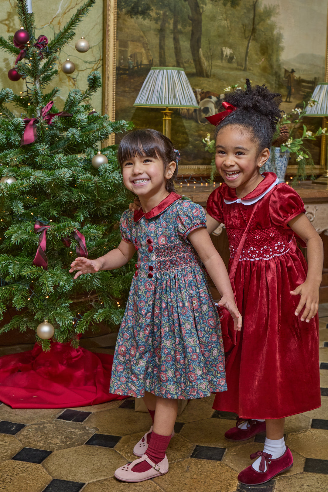 Two girls dressed in holiday dresses in front of christmas tree