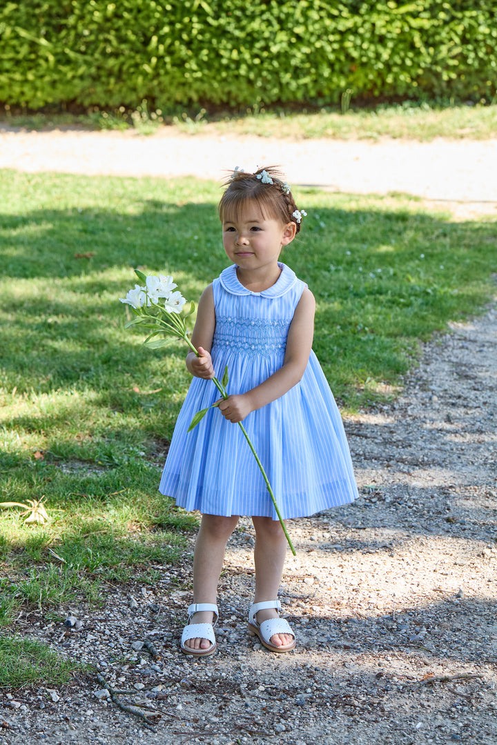 Young girl in a blue dress holding flowers outdoors on a sunny day