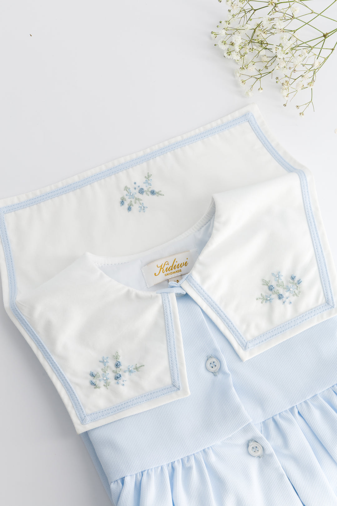 Light blue dress with white collar and floral embroidery on a light gray background