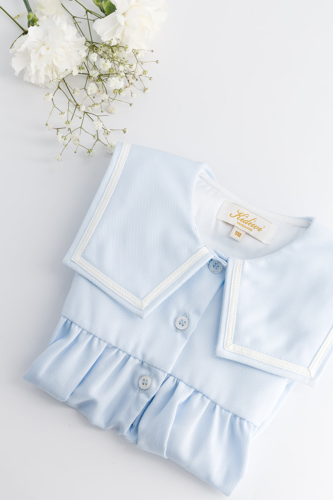 Light blue baby outfit with ruffled details on a white background