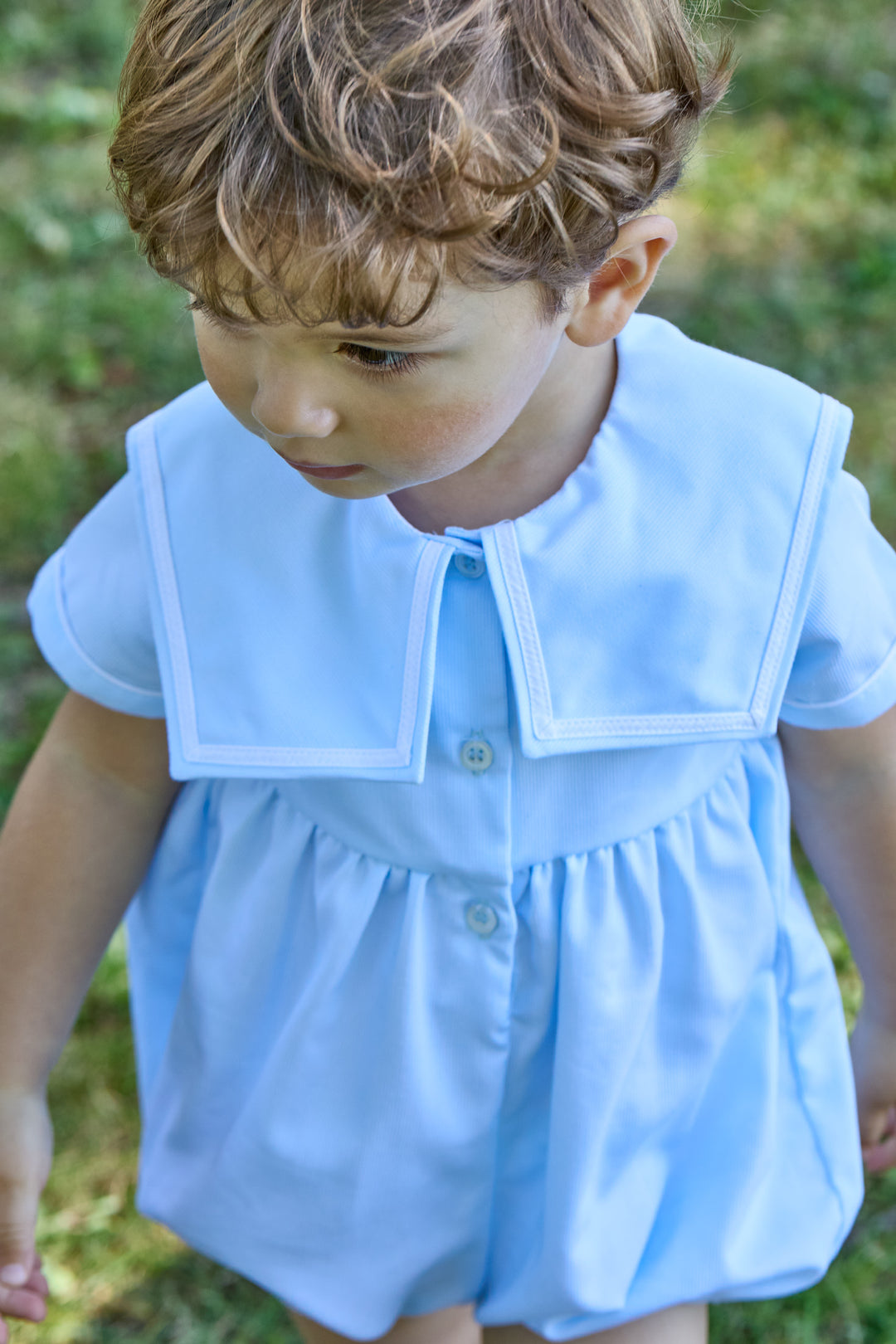 Child wearing a light blue outfit with a collar in an outdoor setting