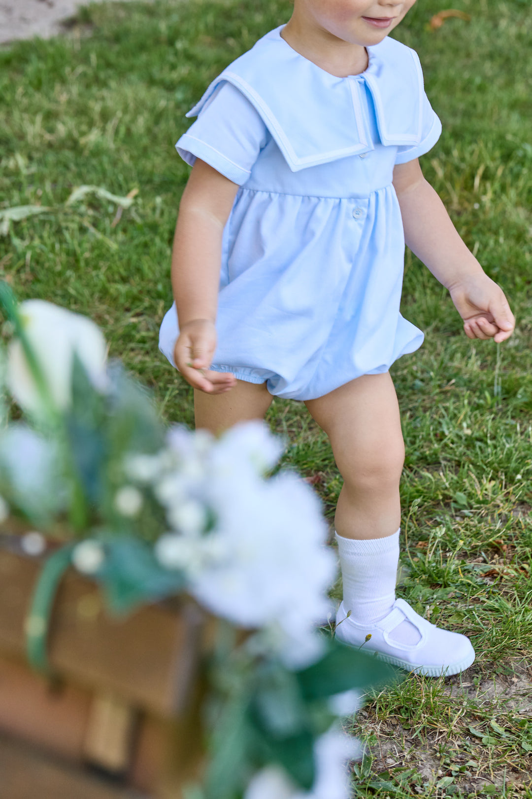 Child wearing a light blue romper with ruffled top in a grassy outdoor setting.