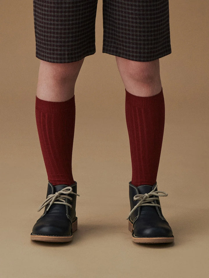Person wearing dark checkered shorts, red knee-high socks, and black shoes on a brown background