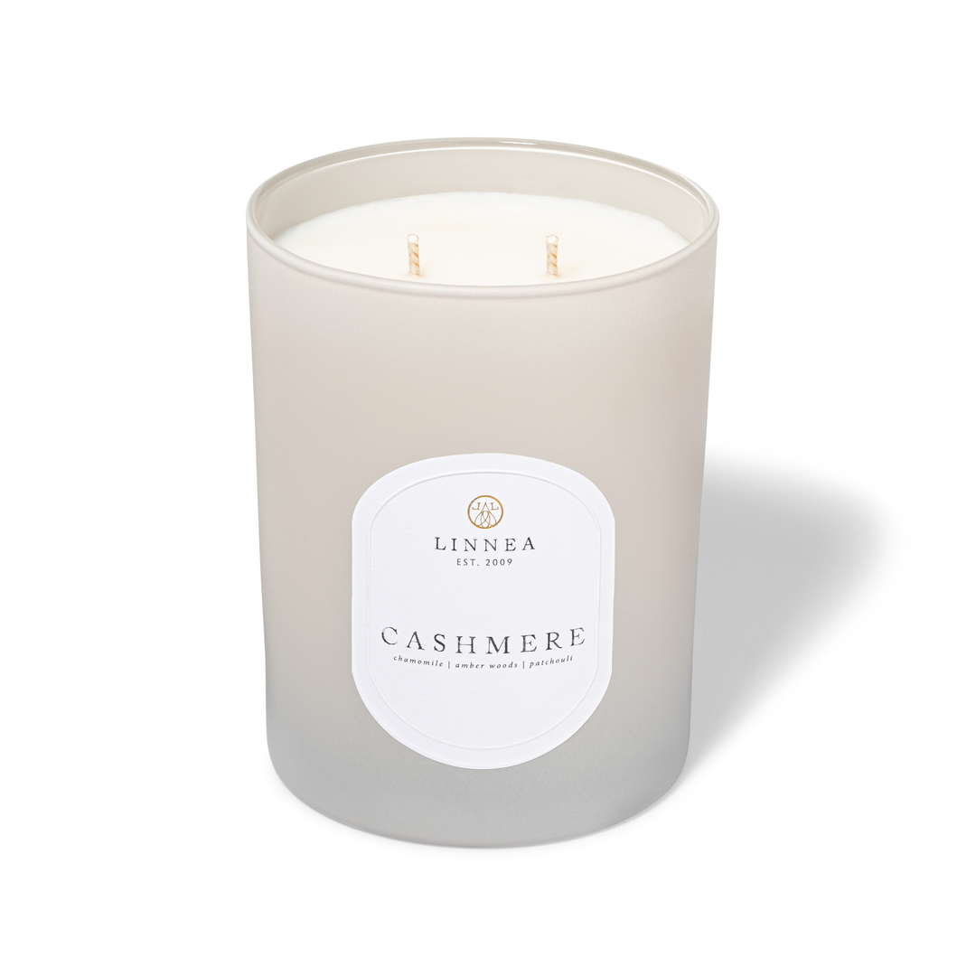 A frosted glass jar candle with two wicks, featuring a white label that reads 'LINNEA EST. 2009' and 'CASHMERE'.
