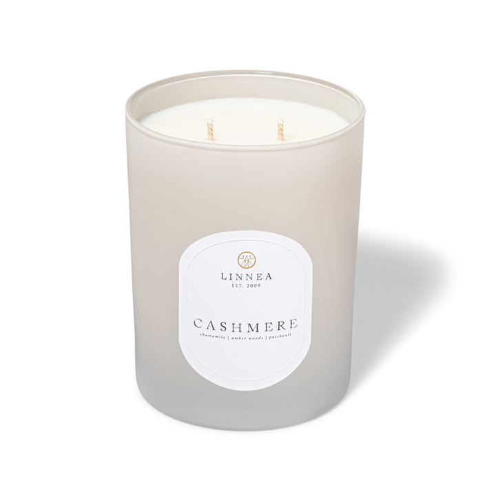 A frosted glass jar candle with two wicks, featuring a white label that reads 'LINNEA EST. 2009' and 'CASHMERE'.
